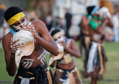 A dancer from Torres Strait Island blows into large cone shell as part of ceremony at BTOF2024